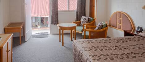 A hotel room with a bed, a chair, a small table, and a window with curtains.