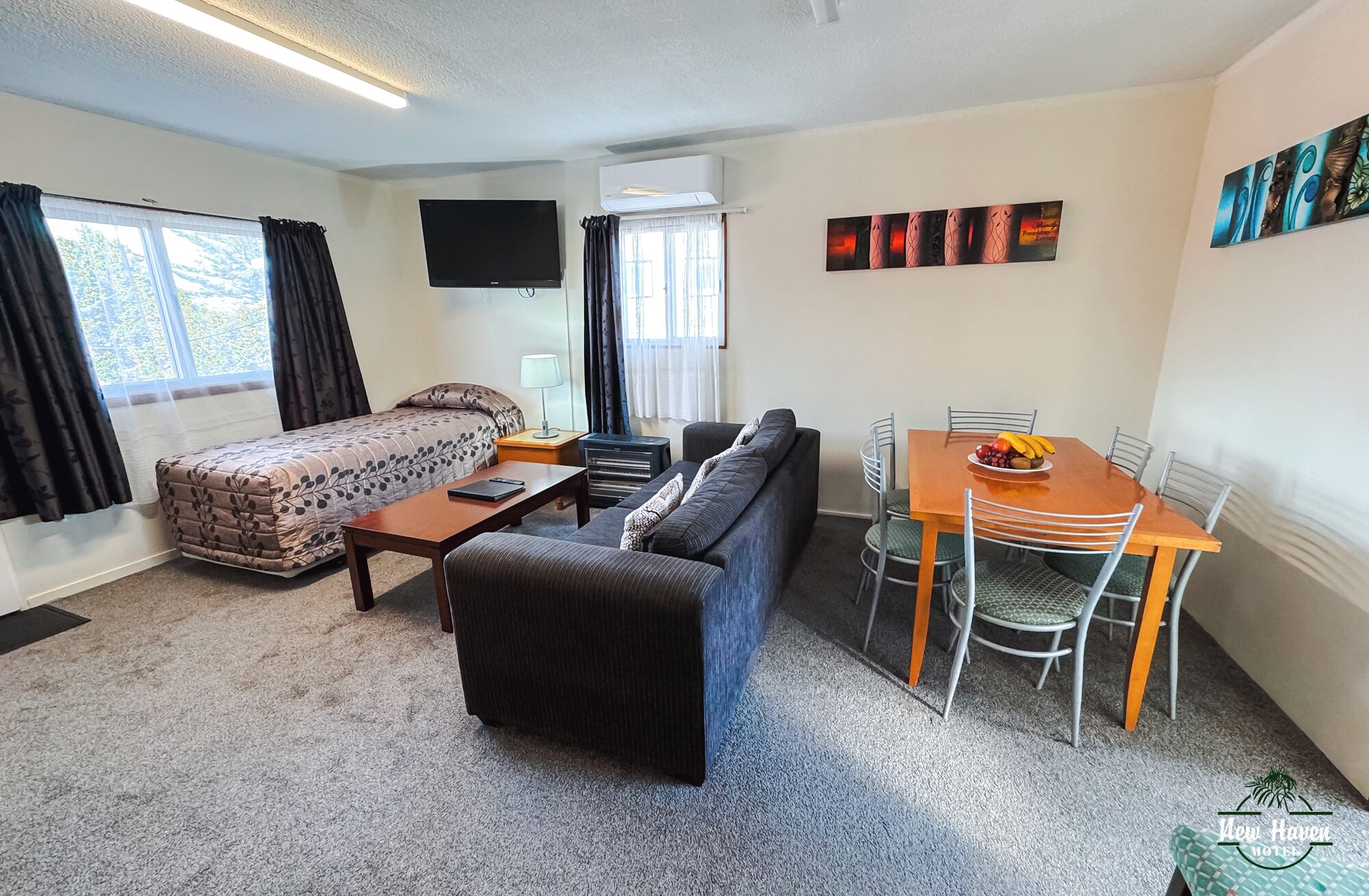 A compact hotel room with a bed, sofa, dining table, chairs, and a TV.