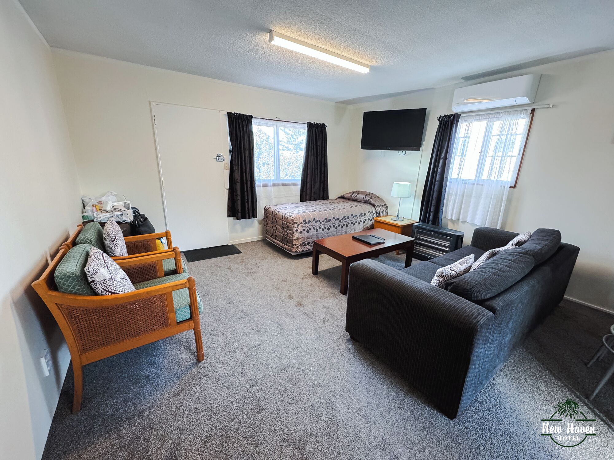 A hotel room with a bed, a sofa, a wooden chair, a small table, and a TV.