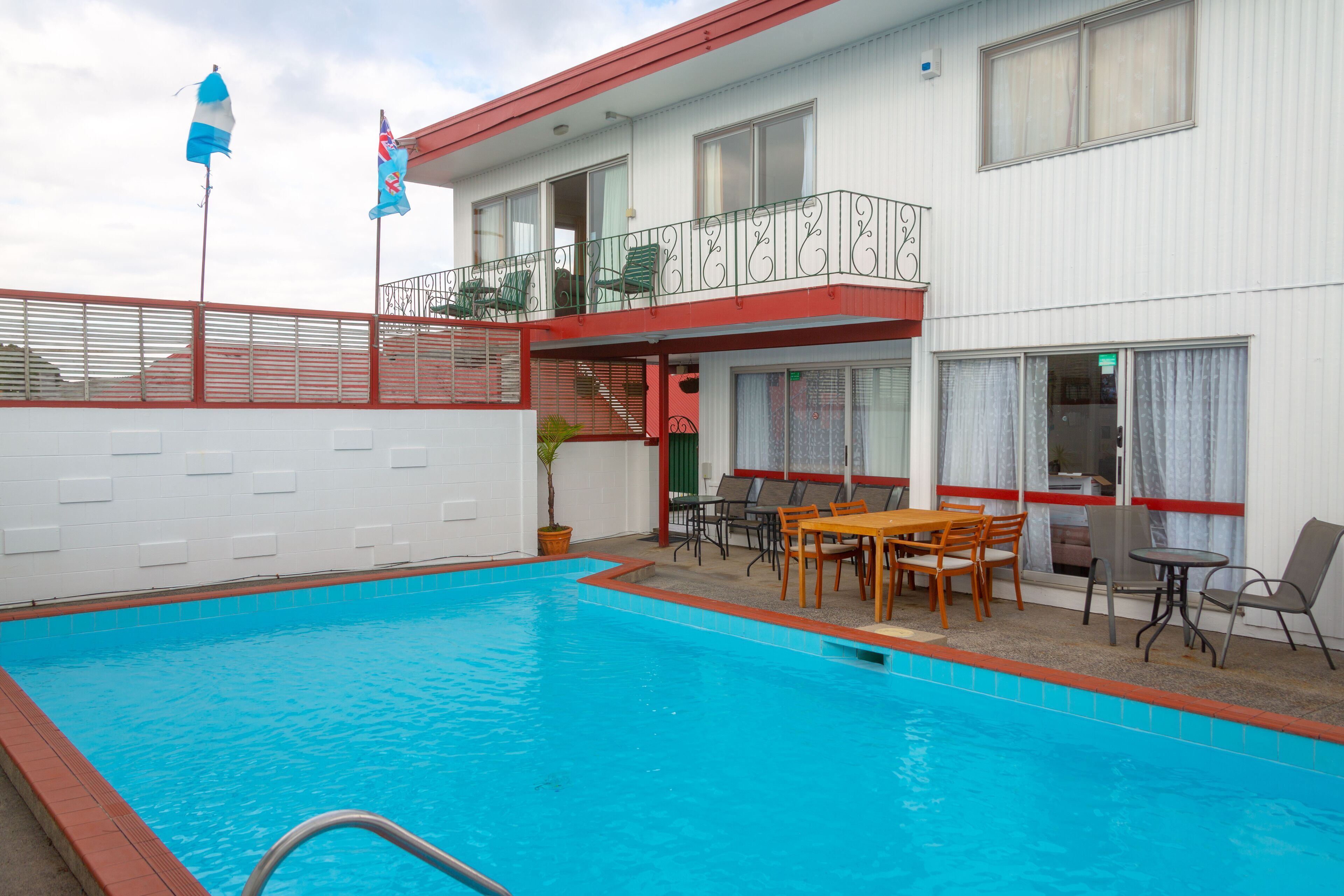 A hotel with a swimming pool, outdoor seating, and a balcony with railings.