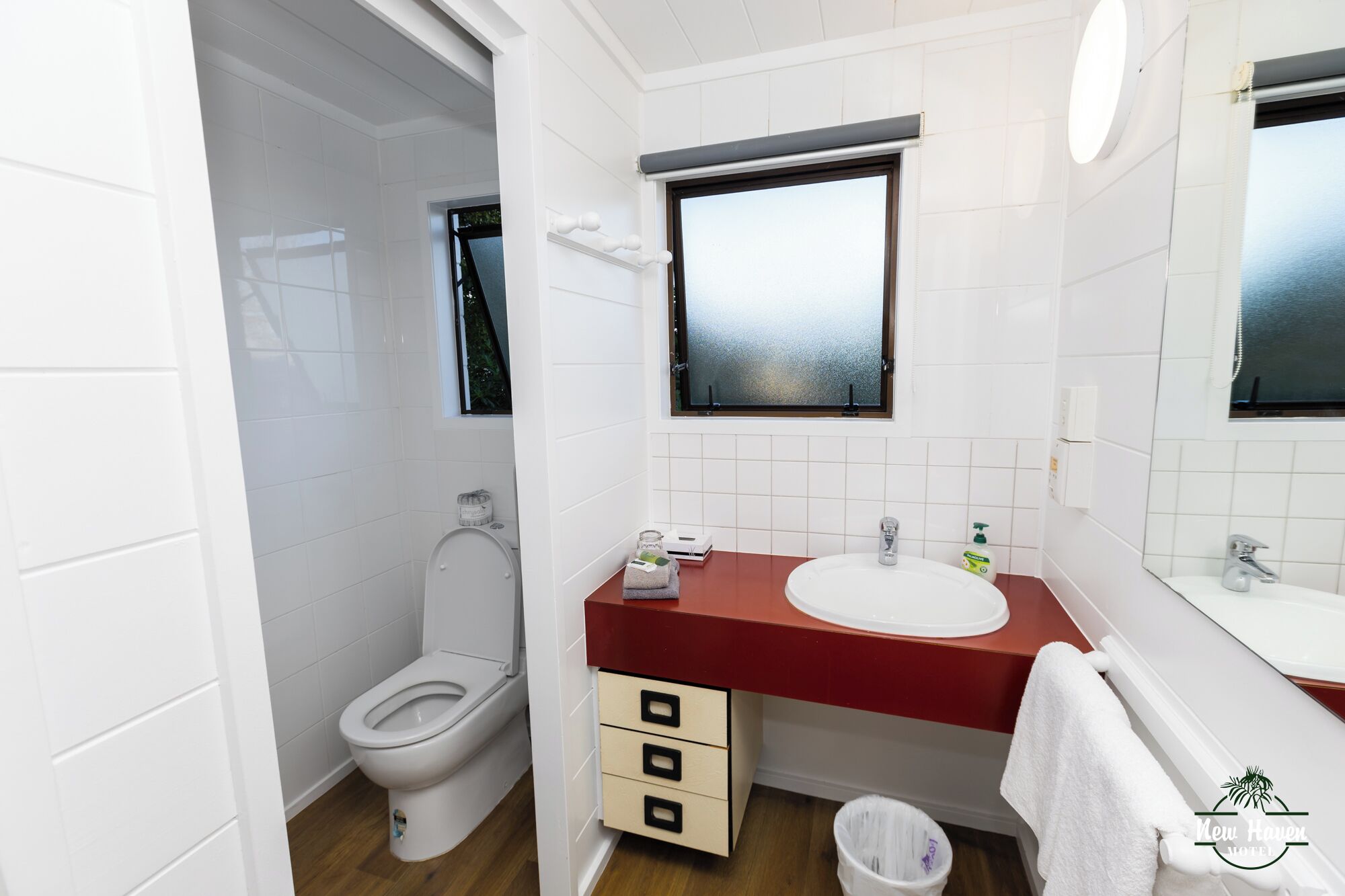A modern bathroom with a white toilet, a red countertop sink, and a window above the sink.