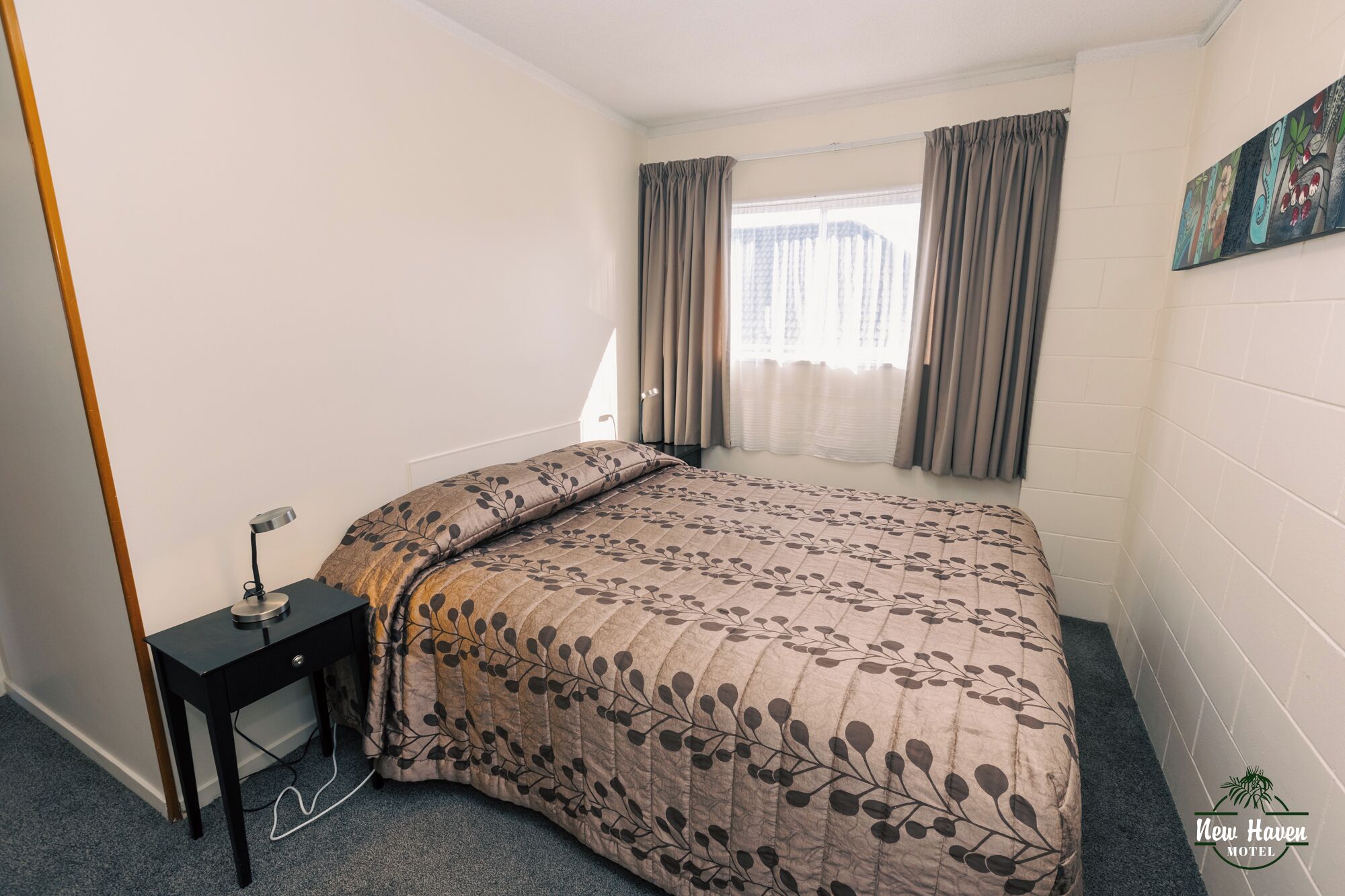 Un dormitorio con cama, mesita de noche, lámpara y ventana con cortinas.