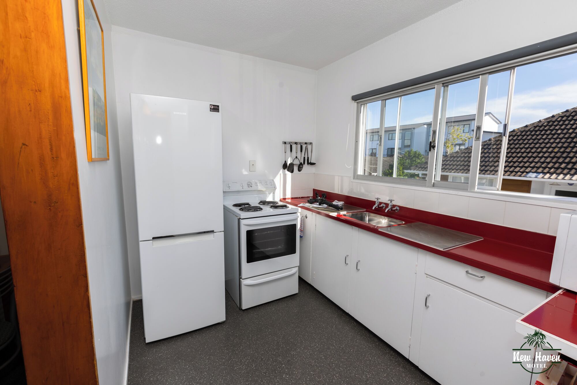 A compact kitchen with a refrigerator, stove, oven, and a red countertop.