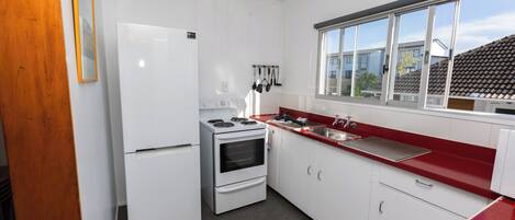 A compact kitchen with a refrigerator, stove, oven, and a red countertop.