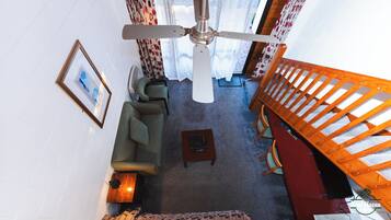 Una sala de estar con ventilador de techo, un sofá, una mesa de centro y una escalera.