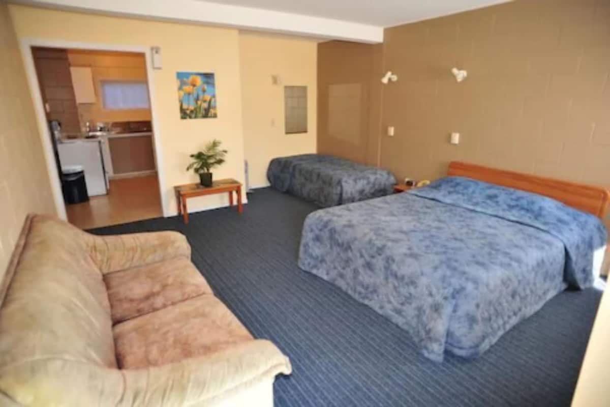 A hotel room with two beds, a sofa, a small table, and a kitchenette in the background.