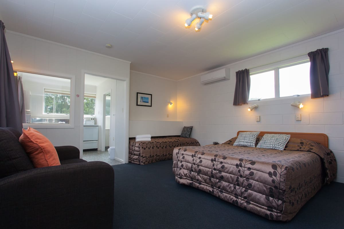 A room with two beds, a sofa, a window with curtains, and an air conditioning unit.