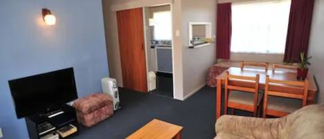 Una sala de estar con televisor, sofá, mesa de madera y un comedor con sillas y una mesa pequeña.