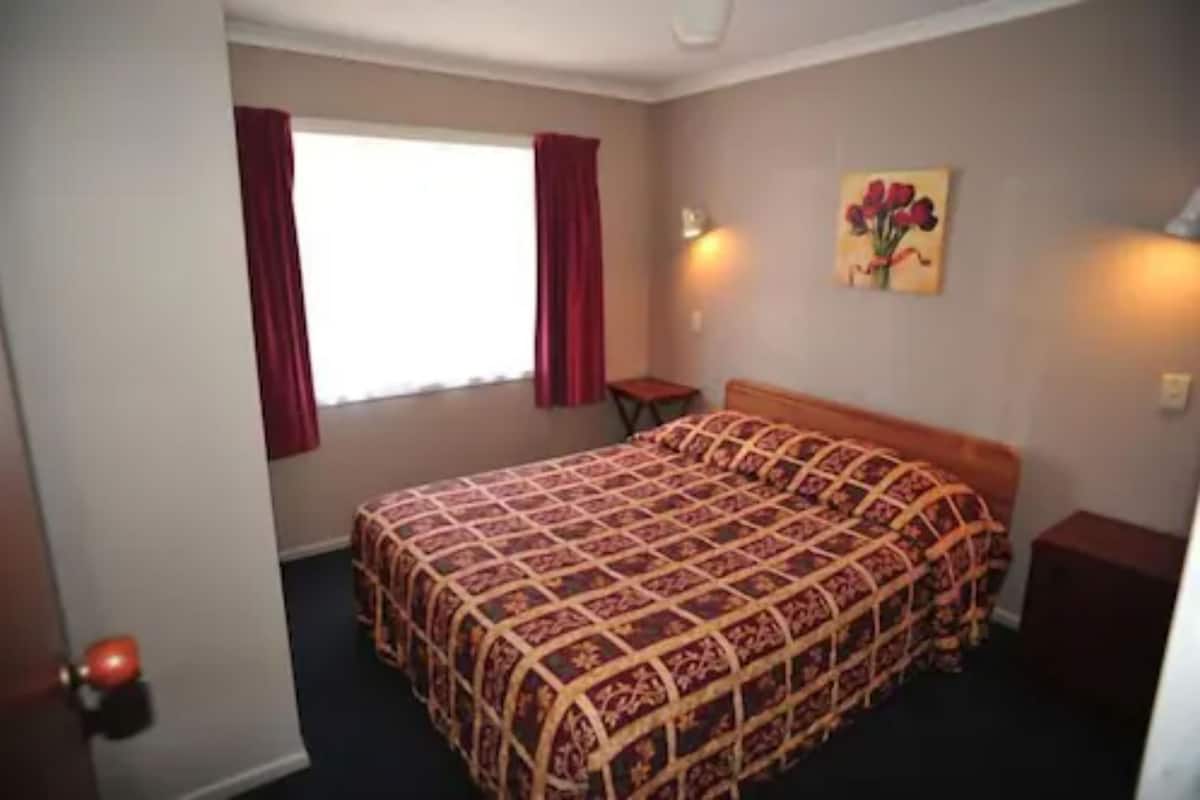 A bedroom with a large bed, a small table, and a painting on the wall.