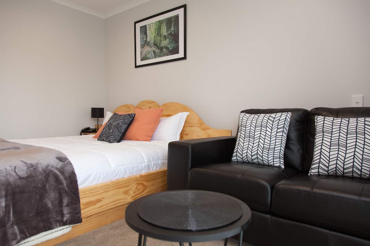 A bedroom with a bed, a black leather sofa, a small round table, and a framed picture on the wall.