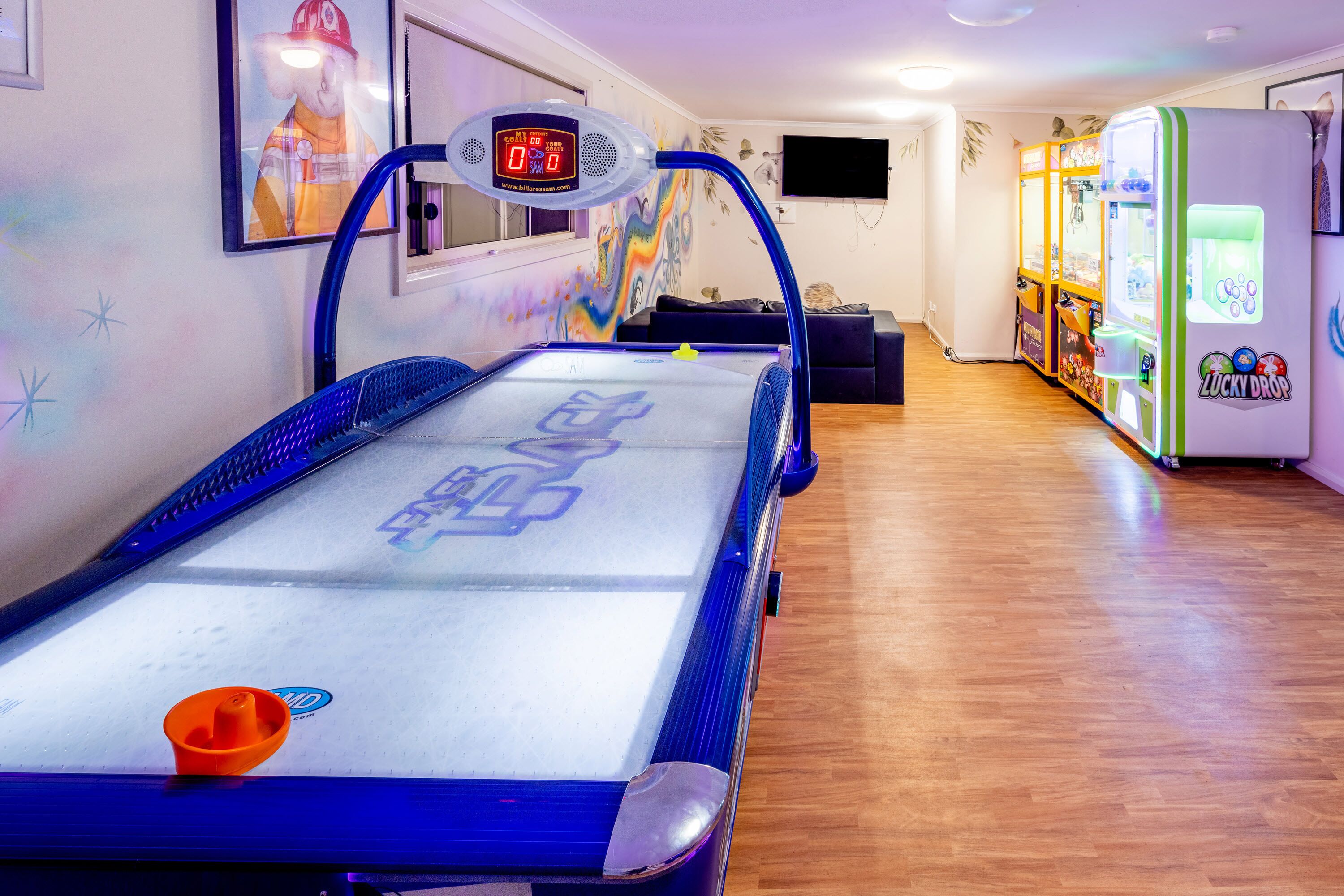 A pool table with a digital scoreboard, arcade games, and a mural on the wall.