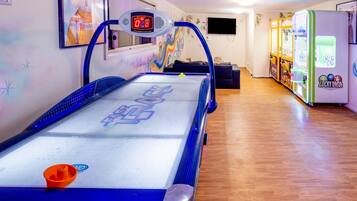 A pool table with a digital scoreboard, arcade games, and a mural on the wall.