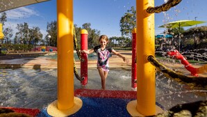 A water play area with a child playing, featuring water jets and a rope obstacle.