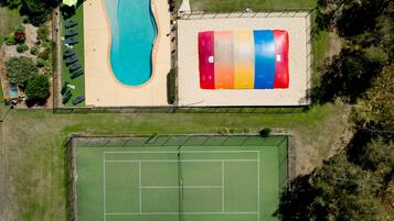 An aerial view of a property with a swimming pool, a tennis court, and a multi-colored sand volleyball court.