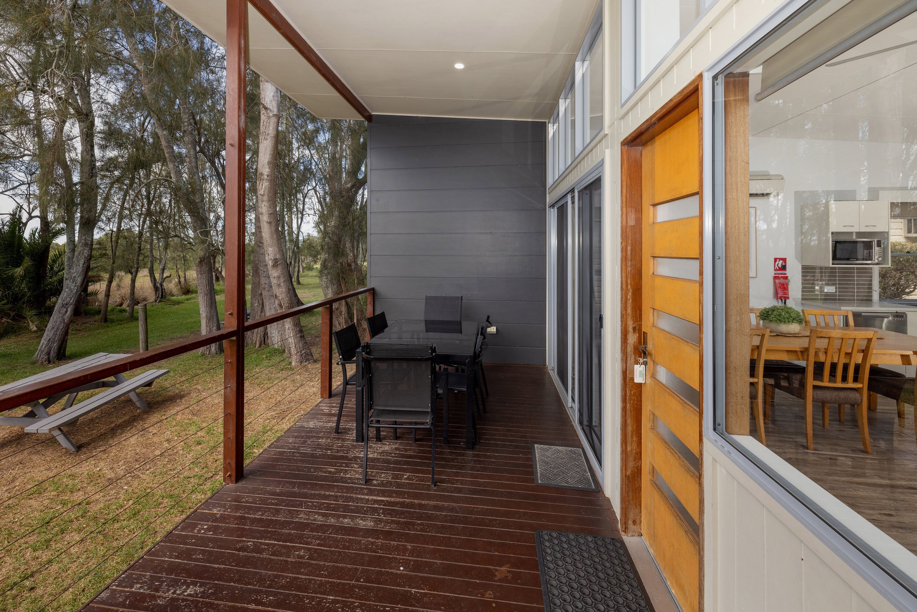 A covered outdoor area with a wooden deck, a table with chairs, and a view of the surrounding trees.