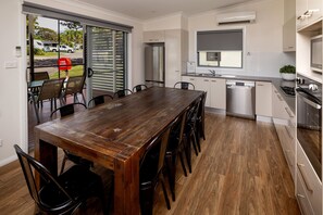 A modern kitchen with a wooden dining table and chairs, a built-in oven, and a dishwasher. - BIG4 Karuah Jetty Holiday Park (Karuah)