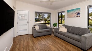A modern living room with two grey sofas, a flat-screen TV, and large windows offering a view of the outdoors.