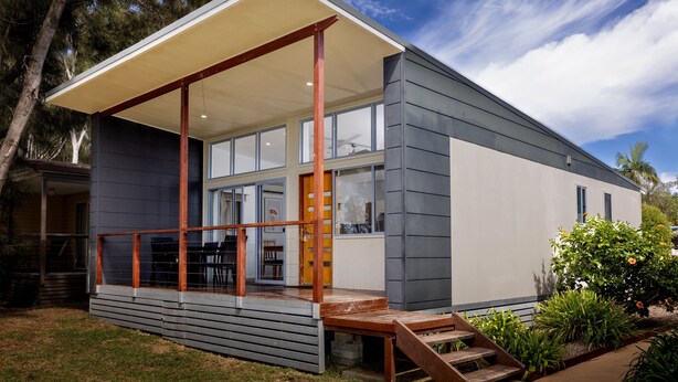 A modern house with a covered porch, large windows, and a staircase leading to the entrance.