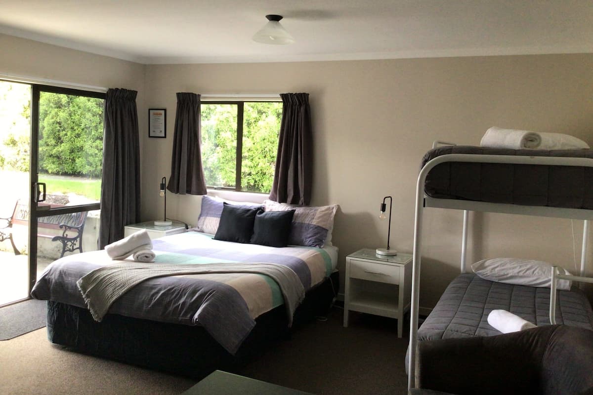 A bedroom with a bed, a bunk bed, a bedside table, a lamp, and a window with curtains.