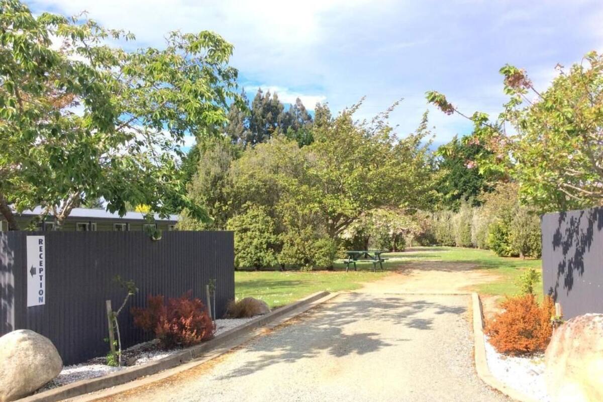 A reception area with a gravel path leading to a building, surrounded by trees and shrubs.