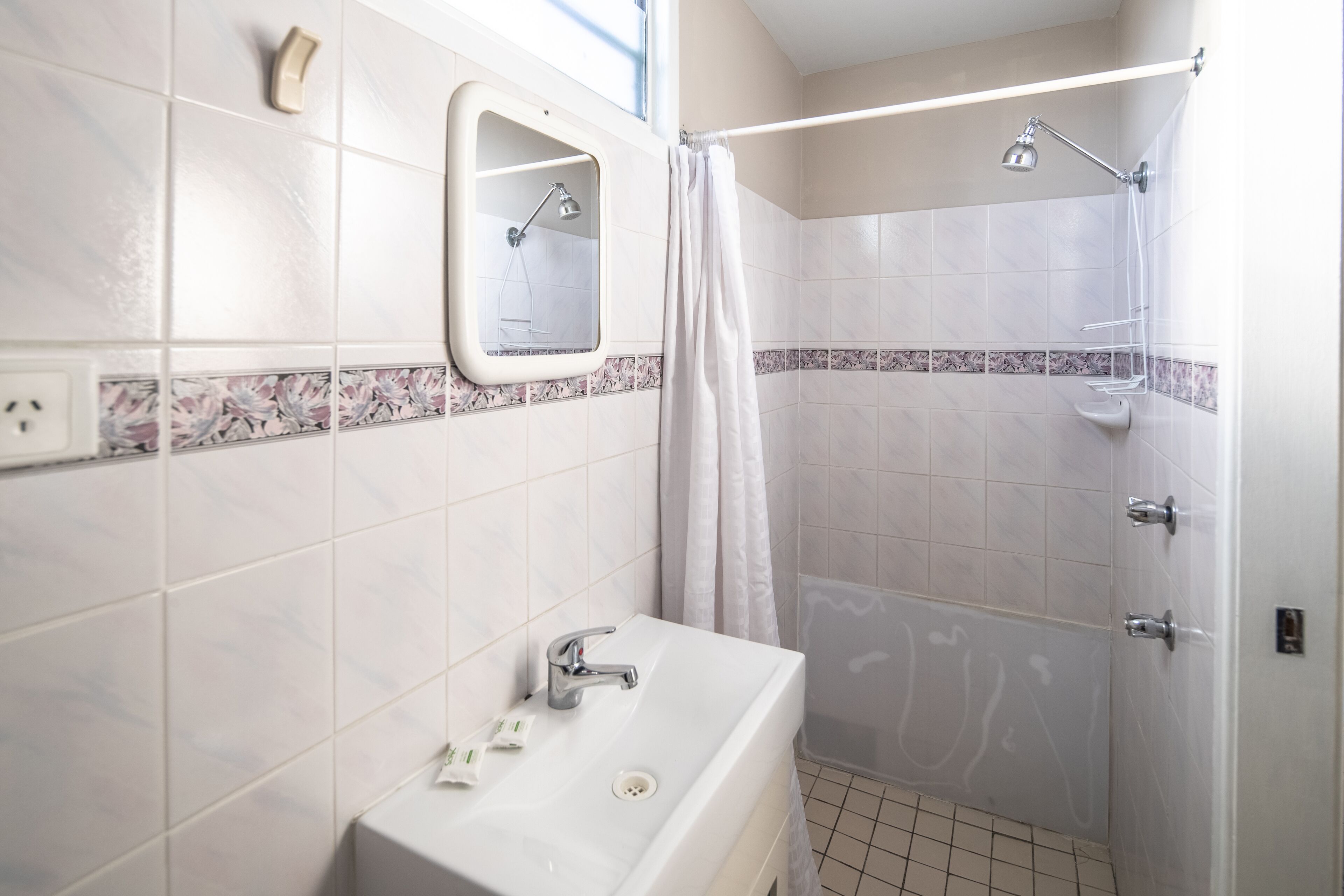 Une salle de bain avec un lavabo, un miroir, une douche et des murs carrelés.