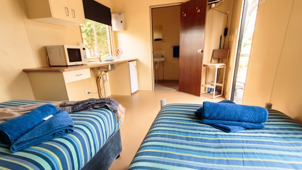 Une chambre d’hôtel avec deux lits, un bureau doté d’un micro-ondes, un petit placard et une salle de bain visible à travers une porte ouverte.