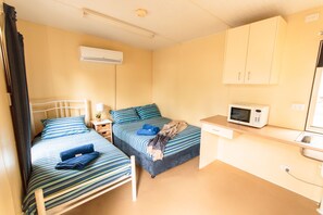 Une petite chambre compacte équipée de deux lits simples, d’un four à micro-ondes, d’une petite table et d’un évier.