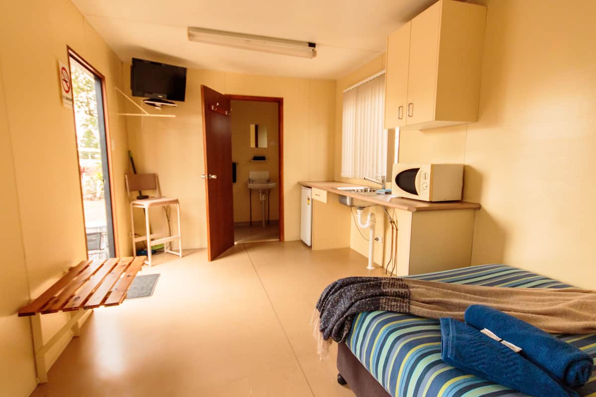 Ein kompaktes Hotelzimmer mit Bett, Schreibtisch, Stuhl, Fernseher und einer Küchenzeile.