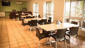Un espace repas avec des tables et des chaises, un coin cuisine avec un téléviseur, et de grandes fenêtres offrant une vue dégagée.