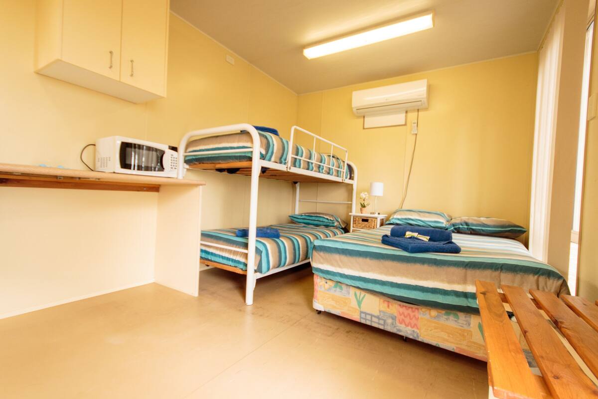 Ein Schlafsaalzimmer mit Etagenbetten, einer Mikrowelle, einem kleinen Tisch und einem Nachttisch.