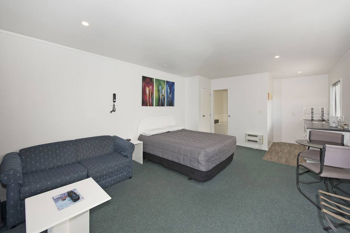 A small, clean room with a bed, a sofa, a desk, and a chair.