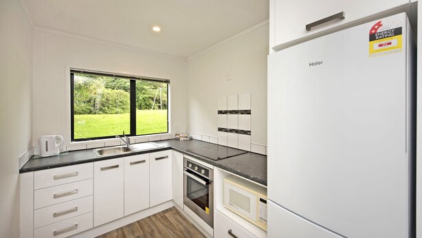 A modern kitchen with white cabinets, a black countertop, and a large window offering a view of greenery. - Camellia Court Motel (Lower Hutt)