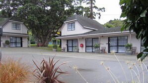A two-story building with a flat roof and large windows. There are potted plants and a statue in the foreground. - Camellia Court Motel (Lower Hutt)