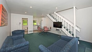 A modern living room with two blue patterned sofas, a dining table with chairs, a kitchen area, and a staircase. - Camellia Court Motel (Lower Hutt)