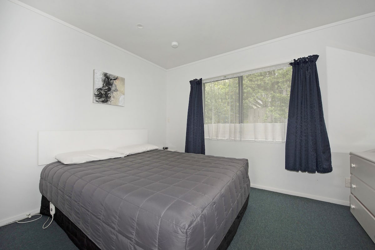 A bedroom with a bed, a window with curtains, a dresser, and a painting on the wall.