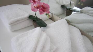 Un baño con toallas blancas apiladas y un jarrón con orquídeas rosas.
