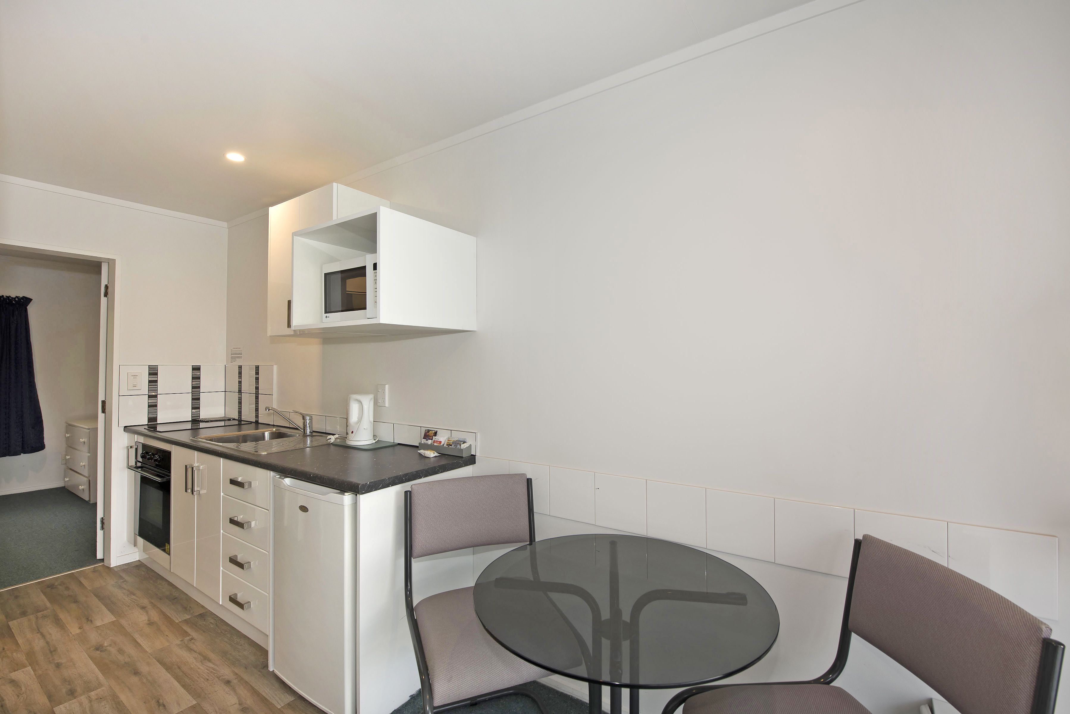 A compact kitchen with a built-in oven, a sink, and a microwave. There is a round table with two chairs in the center.