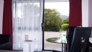 A room with a bed, a desk, a chair, a table, and a view of a garden through a glass door. - Camellia Court Motel (Lower Hutt)