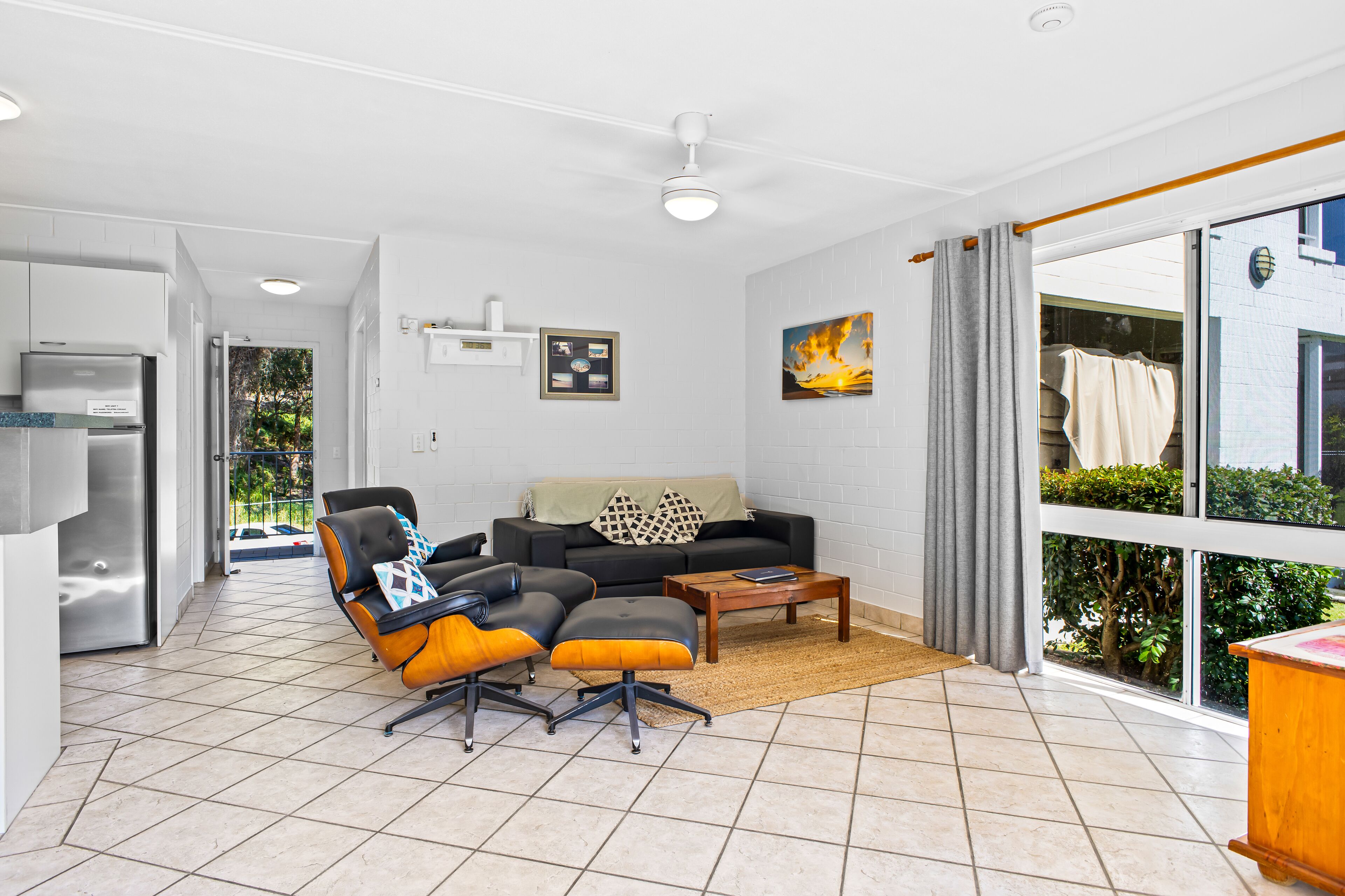 A modern living room with a sofa, two armchairs, a coffee table, and a view of greenery through large windows.