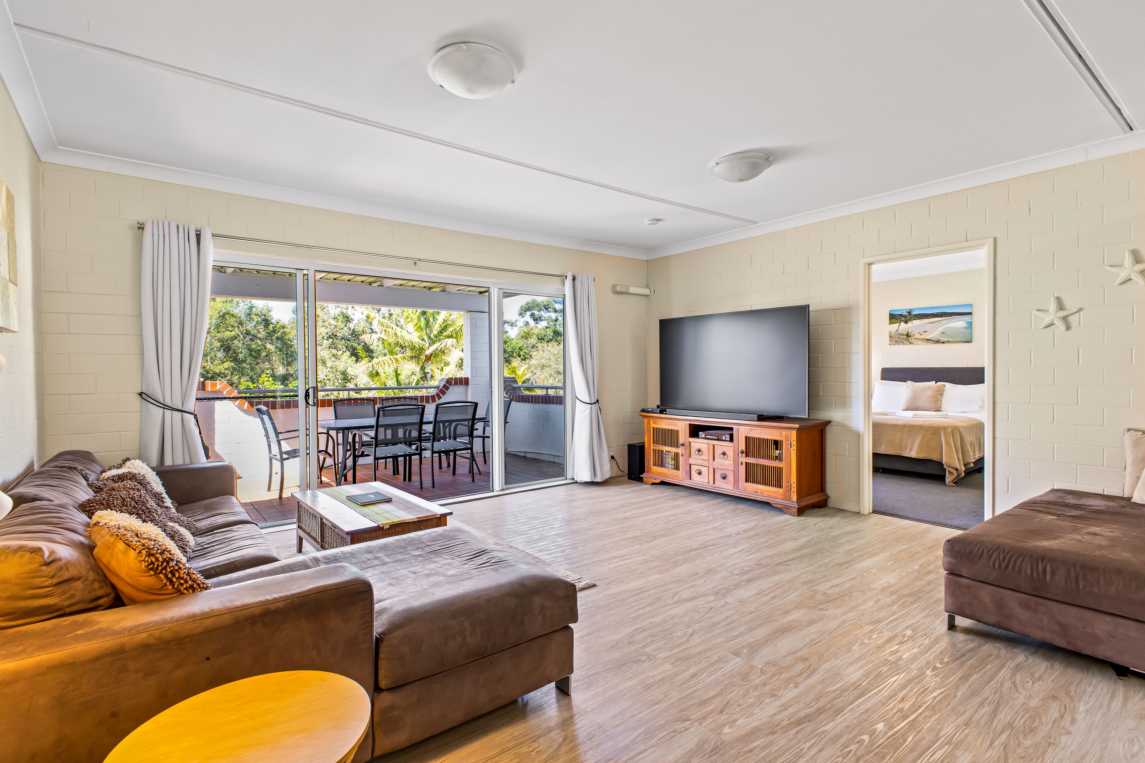 A spacious living room with a sofa, TV stand, and a sliding glass door leading to an outdoor patio.