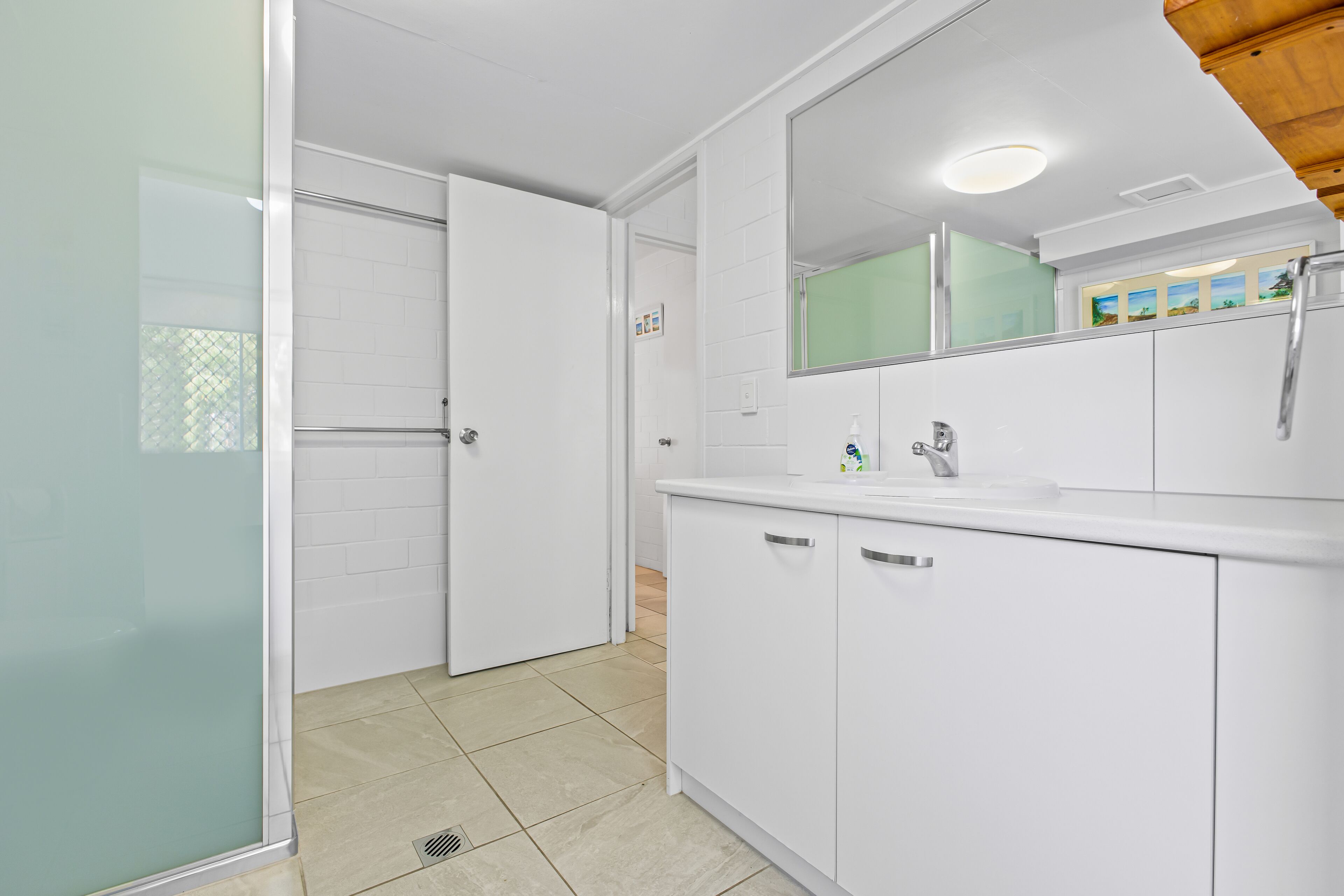 A modern bathroom with white cabinetry, a glass shower enclosure, and a large mirror above the sink.