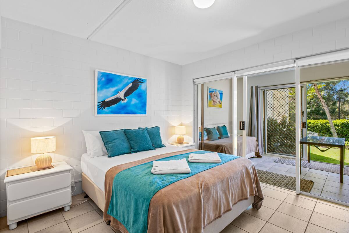 A bedroom with a bed, nightstands, and a view of the outdoors.