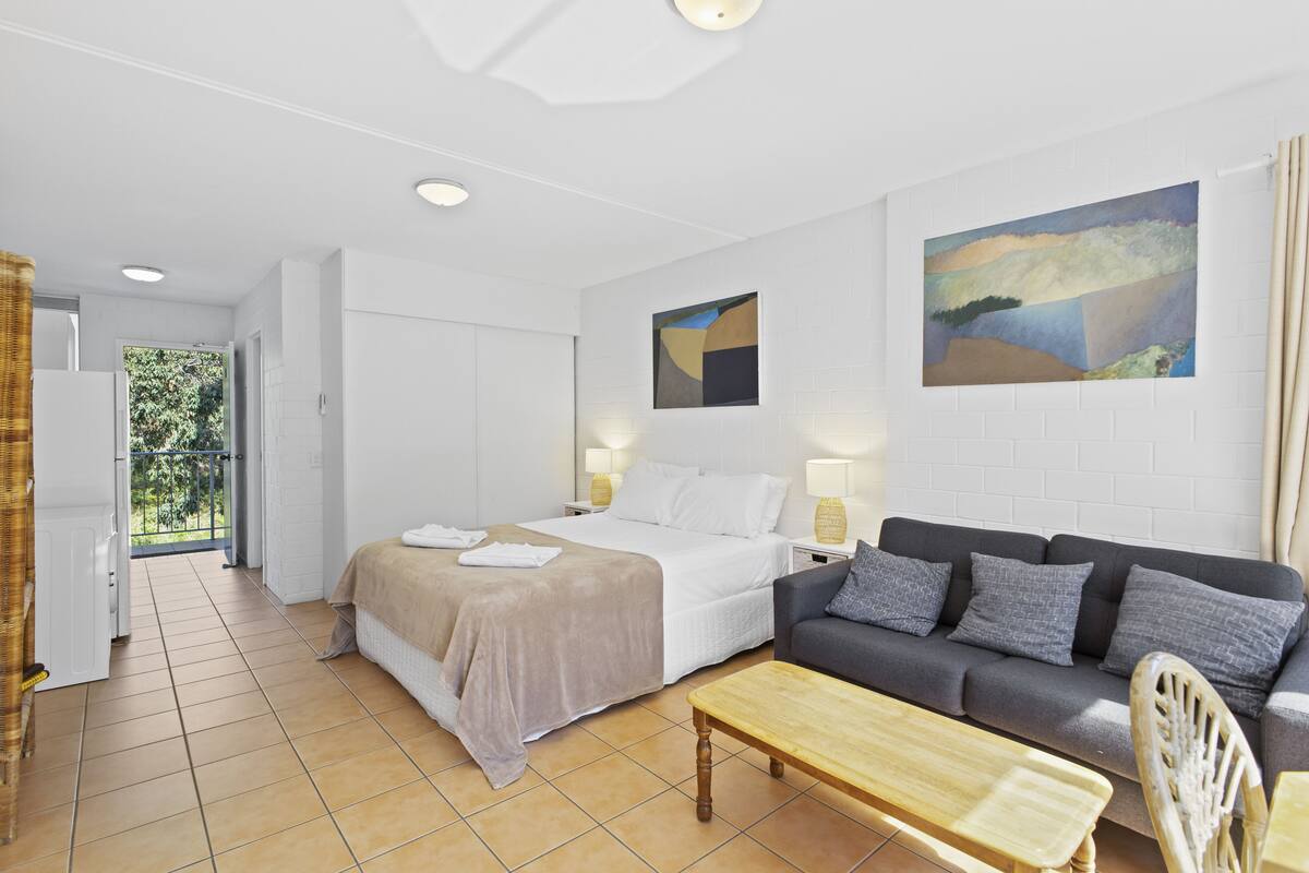 A hotel room with a bed, a sofa, a wooden table, and a painting on the wall.