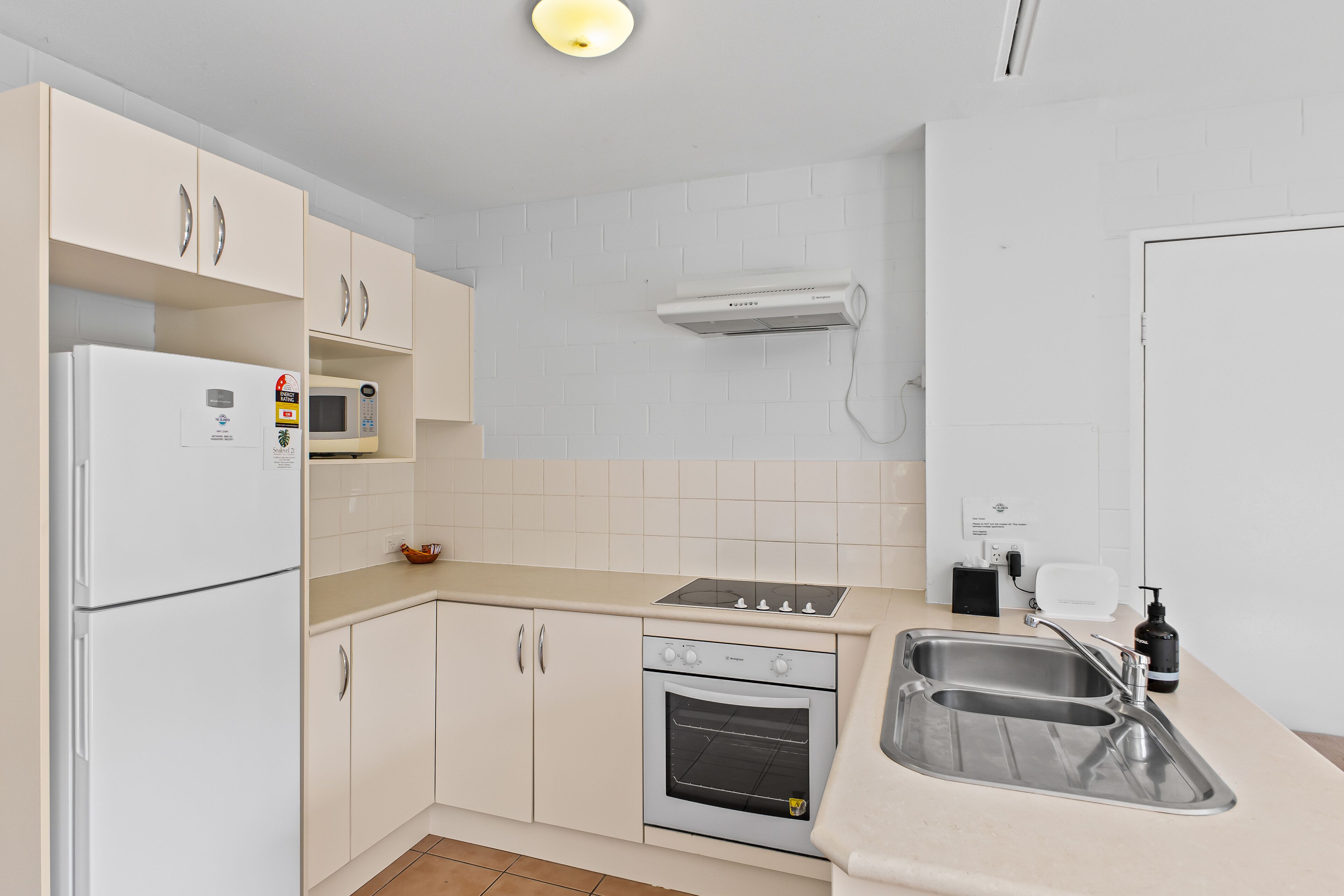 Una cuina amb armaris blancs, un forn de microones integrat, una placa de cocció i un rentaplat.