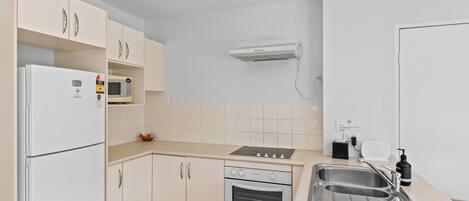 Una cuina amb armaris blancs, un forn de microones integrat, una placa de cocció i un rentaplat.