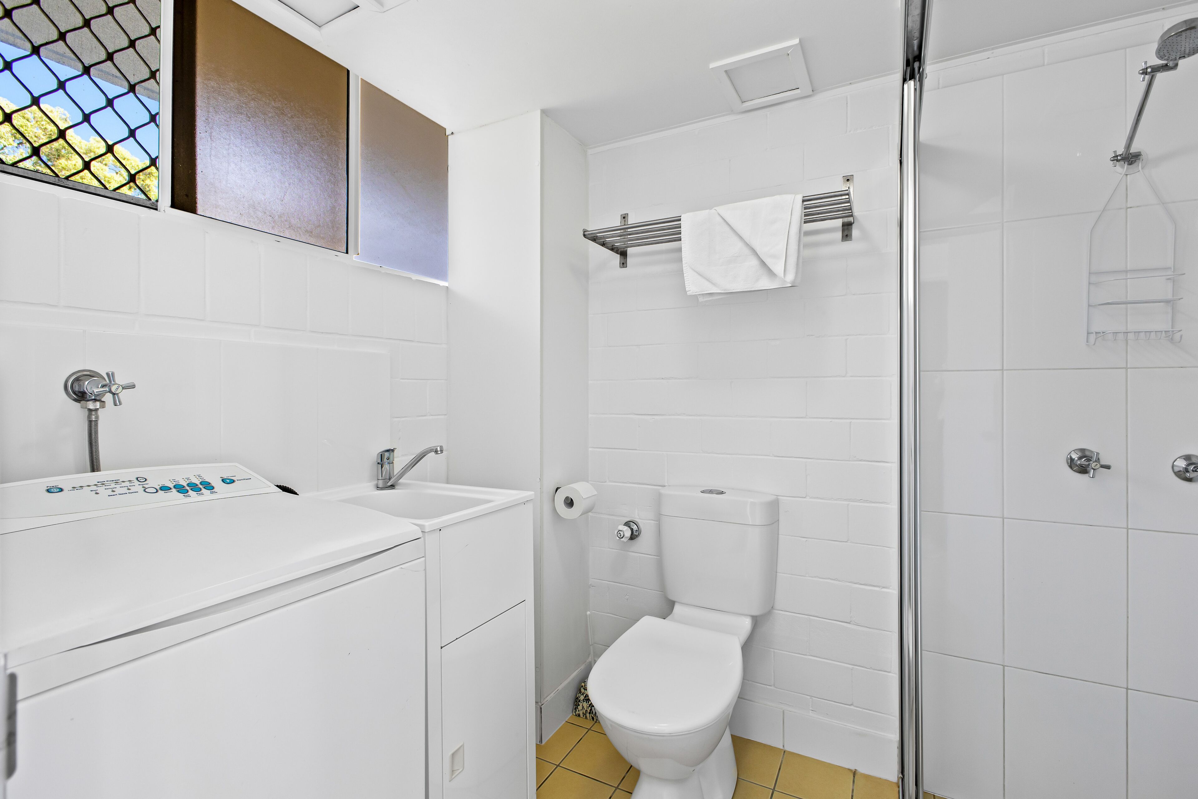 A bathroom with a washing machine, toilet, and shower.