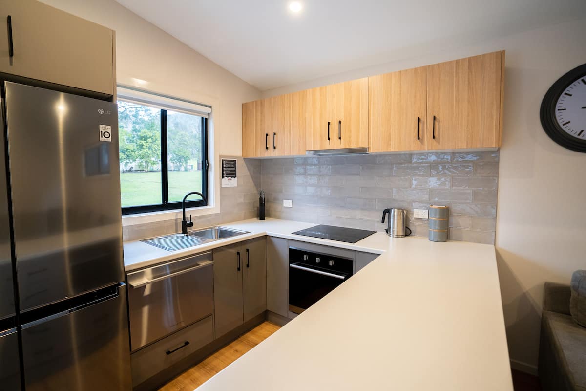 A modern kitchen with stainless steel appliances, wooden cabinets, a built-in oven, and a large window.