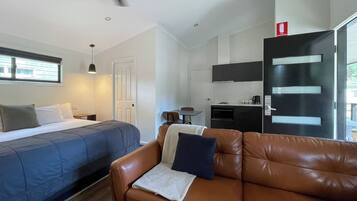A modern hotel room with a bed, a brown leather sofa, a kitchenette, and a ceiling fan.