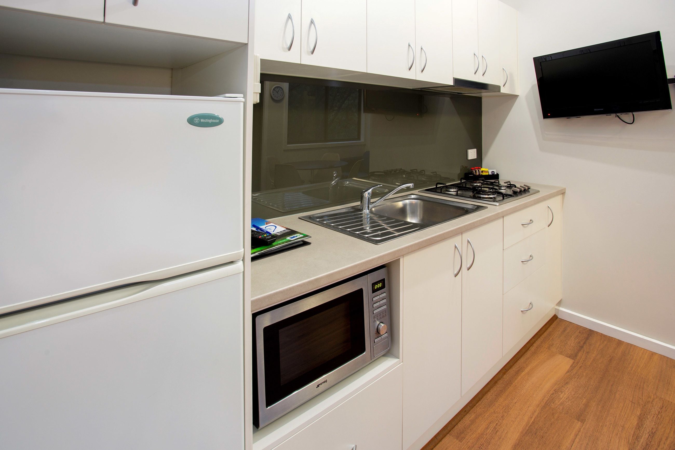 Une cuisine compacte équipée d’un four à micro-ondes, d’une cuisinière, d’un évier et d’un téléviseur à écran plat fixé au mur.