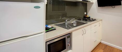 A compact kitchen with a microwave, stove, sink, and a flat-screen TV mounted on the wall.